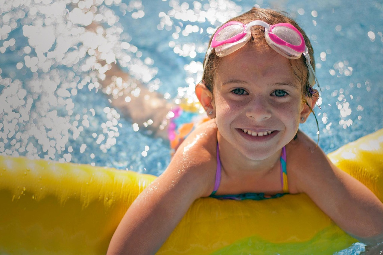 Swimming pool safety image of a girl with floating device in pool with goggles on and smiling